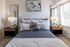 Inviting bedroom with elegant decor featuring a plush bed with layered pillows, stylish bedside lamps, and vibrant wall art under natural light.