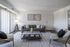 Modern living room with a sleek grey sofa, stylish armchairs, and a chic glass coffee table. Bright and inviting, featuring tasteful artwork and warm lighting.