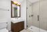 Modern bathroom with elegant wood accents, featuring a sleek vanity, spacious mirror, and glass-enclosed shower.