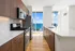 Modern kitchen with sleek wooden cabinetry, stainless steel appliances, and stunning ocean view through large windows.