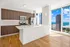 Modern kitchen with sleek wooden cabinetry and stainless steel appliances, offering panoramic city and lake views through large windows.
