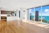 Modern apartment with floor-to-ceiling windows offering breathtaking city and lake views, featuring a sleek kitchen with stainless steel appliances and elegant wood flooring.