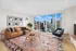Luxurious living room with modern decor, large windows offering stunning cityscape views, cozy seating, and vibrant patterned rug.