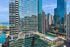 Luxurious high-rise with stunning glass facade offering panoramic views of the city skyline and shimmering waterfront, featuring a serene rooftop pool and lush green terrace.