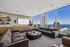 Elegant living room with panoramic city views, featuring modern gray sofas, stylish wooden cabinetry, and contemporary decor accents against a backdrop of a stunning skyline.