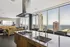 Luxurious open-concept apartment featuring a sleek modern kitchen with marble countertop, adjacent to a stylish living area boasting stunning city and lake views through expansive floor-to-ceiling windows.