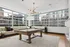 Luxurious apartment recreation room with a modern pool table, plush seating, and stunning cityscape views through expansive windows.