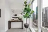 Bright modern apartment corner with a large window view showing cityscape, stylish desk setup, and vibrant indoor plant for a serene urban living space.