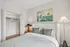 Charming bedroom with a cozy bed and elegant bedside lamps, featuring an open closet and serene wall art.