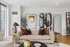 Modern living room featuring a chic beige sofa with elegant pillows, surrounded by stylish decor elements, including a unique black shelving unit with artistic vases and books, all set against a backdrop of city views through expansive windows.