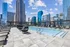 Luxurious rooftop pool with sleek lounge chairs, surrounded by towering city skyscrapers and a vibrant blue sky backdrop.