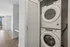 Modern apartment with in-unit laundry featuring stacked washer and dryer, bright natural lighting, and elegant hardwood flooring.