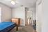Inviting bedroom with plush carpet, modern dresser, and a view into a bright living space through an open doorway.