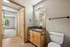 Modern bathroom with granite countertop, sleek fixtures, and warm wooden cabinets opening to a cozy carpeted bedroom in a sunlit apartment.