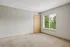 Bright and airy room with plush carpet, large window, and simple wood accents, offering a serene view of lush greenery.
