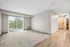 Bright, spacious living room with elegant hardwood floors and plush carpet, featuring large windows with vertical blinds and a serene view of greenery.