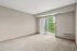 Bright and airy apartment room with plush carpet, sliding glass doors, and a scenic balcony view.