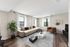 Elegant living room with large windows, a plush L-shaped sofa, modern decor, and a cozy armchair on stylish wood flooring.