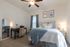 Inviting bedroom with cozy decor, featuring a comfortable bed with soft blue and white linens, a stylish desk with a mirror, and elegant artwork on the walls. Perfectly illuminated by gentle lighting.