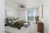 Modern bedroom with a cozy ambiance, featuring a king-size bed dressed in olive green bedding, stylish gray ottomans, and abundant natural light through large windows.
