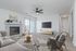 Modern living room with a cozy fireplace, sleek ceiling fan, and a large TV, beautifully furnished with a plush sofa and armchairs, set against stylish décor in a bright, airy space.