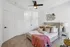 Inviting bedroom with a plush bed adorned with decorative pillows and a vibrant pink throw, illuminated by a modern ceiling fan and complemented by a stylish geometric wall mirror.