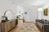 Bright and inviting living room with stylish decor, featuring a cozy gray sofa, modern wooden console, and a sleek floor lamp. Open layout leading to a charming white kitchen.