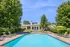 Inviting outdoor pool area with modern recliners, lush green trees, and a stylish clubhouse under a clear blue sky.