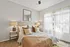 Bright and welcoming bedroom featuring soft beige tones, a cozy bed with plush pillows, ambient lighting, and airy curtains.