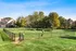 Lush community dog park with agility equipment and picnic tables, surrounded by scenic greenery and charming townhouses.