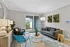 Bright and inviting living room with modern decor, featuring a gray sofa, vibrant blue chairs, and lush green accents, opening to a garden view through sliding glass doors.