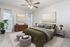 Elegant bedroom with a modern touch, featuring a plush olive-green bed, contemporary furniture, and serene artwork, accentuated by ample natural light.