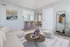 Stylish living room featuring a cozy beige sofa, modern round coffee table, and open view to dining and kitchen area with bar stools.