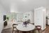 Bright and modern living area with a cozy white sofa, elegant decor, and a dining table with a marble top. The room features a large window with vertical blinds and stylish wooden furniture, offering a welcoming and spacious atmosphere.