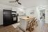 Bright and modern kitchen with a sleek black refrigerator, stylish wooden island, and cozy breakfast bar stools, leading to a sunlit bedroom.