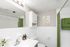 Bright and modern bathroom with elegant white tiles, stylish green accents, and artistic decor, featuring a spacious mirror and sleek fixtures for a refreshing ambiance.