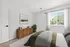 Bright and inviting bedroom with a modern wooden dresser, lush greenery, and large window overlooking a scenic view.