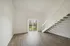 Bright, open-concept living area with modern wooden flooring and sleek staircase leading to a loft, featuring a large glass door opening to a scenic balcony view.