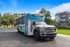 Vibrant community shuttle bus parked near modern apartments, surrounded by lush greenery and clear blue skies.