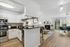 Modern open-concept kitchen and living area with sleek white cabinetry, stainless steel appliances, and stylish decor. Features a cozy fireplace and a bright dining space with garden views.