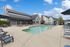 Inviting outdoor pool area with stylish loungers and shaded seating, set against charming residential architecture and bright blue skies.