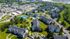 Scenic aerial view of a vibrant residential community featuring modern apartments, lush greenery, a sparkling pool, and tennis courts, offering an idyllic suburban lifestyle.