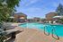 Charming outdoor pool area with sunny lounging spaces, surrounded by lush greenery and comfortable seating at a modern apartment complex.