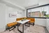 Inviting dining nook with chic white table and modern orange seating, accented by natural light from large window and stylish artwork on the wall.