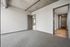 Modern apartment featuring an empty room with gray carpet, exposed concrete ceiling, and a view into a spacious walk-in closet.