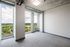 Bright modern room with floor-to-ceiling windows offering panoramic views of lush greenery and cityscape, featuring industrial-style ceilings and neutral carpet.