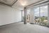 Modern apartment with large windows offering stunning cityscape views, featuring minimalist design and industrial-style concrete ceiling.