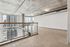 Modern industrial loft space with large windows and city views, featuring exposed concrete ceiling and ductwork.