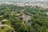 Scenic aerial view of a lush apartment complex surrounded by vibrant greenery, featuring spacious parking lots and close proximity to a vibrant shopping center.