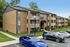 Charming brick apartment building with private balconies, surrounded by lush greenery and ample parking space.